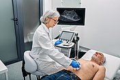 Hier sieht man eine Ärztin, die mit einem Ultraschall die Bauchorgane eines Patienten, der auf einer Liege liegt, untersucht. Die Ultraschalluntersuchung wird auch allgemein Sonografie genannt.