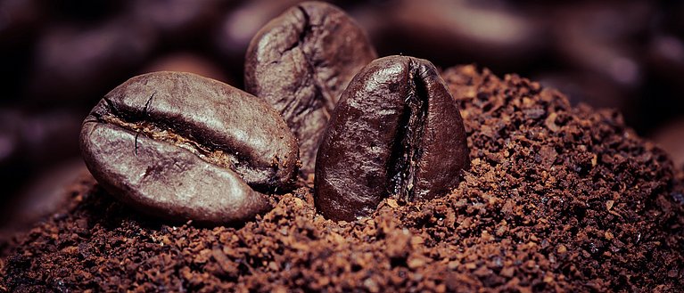Hier sieht man Kaffeekohle und drei einzelne Kaffeebohnen oben auf liegend.